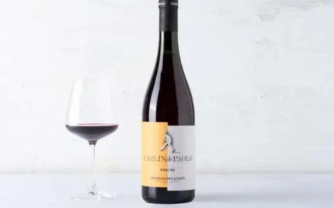 Calice di vino rosso accanto a una bottiglia di Grignolino d'Asti Carlin de Paolo. Un vino che ricorda il barbera vitigno per la sua vivacità.