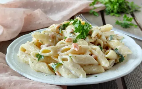 Piatto di pasta panna e salmone, guarnito con prezzemolo fresco, servito su un piatto bianco.