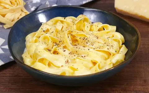 Un piatto di fettuccine alfredo fumanti, condite con una cremosa salsa al parmigiano e pepe nero.
