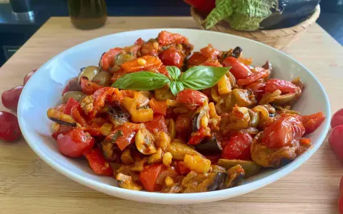 Caponata siciliana ricetta della nonna: un piatto colorato con melanzane, peperoni, pomodorini e basilico, pronto per essere gustato.