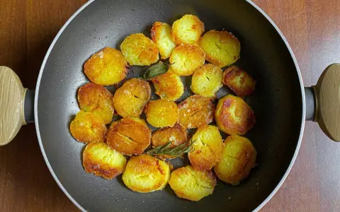 Patate dorate e croccanti in padella, pronte per deliziose ricette con patate. Un rametto di rosmarino aggiunge profumo.