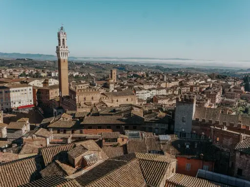 Vista aerea di Siena, con la Torre del Mangia in primo piano. Un'idea per cosa vedere in Toscana in 2 giorni, tra tetti in cotto e colline nebbiose.