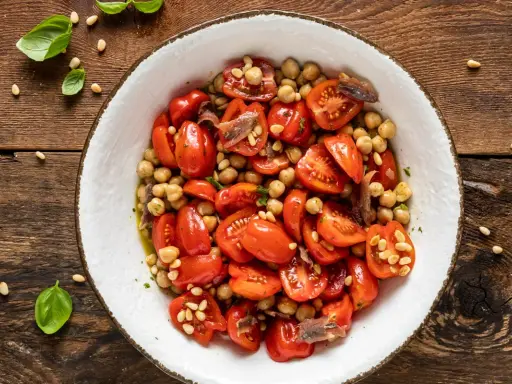 Insalata di ceci e pomodorini, un'idea fresca per le tue ricette con farina di ceci. Guarnita con pinoli e acciughe.