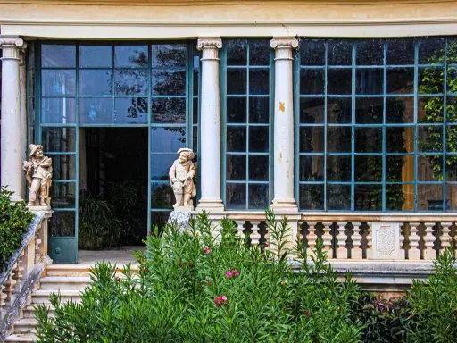 Statue di nani custodi di un giardino lussureggiante sui Colli Berici, con un'elegante serra sullo sfondo.