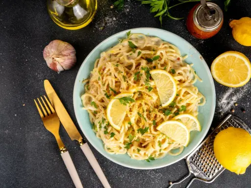 Spaghetti cremosi con un profumo agrumato, guarniti con fette di limone fresco e prezzemolo. Un piatto di pesto al limone che invita a gustare la freschezza.