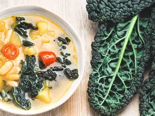 Zuppa ricca con fagioli, pomodoro e il sapore intenso del cavolo nero. Accanto, una foglia di cavolo nero fresca.