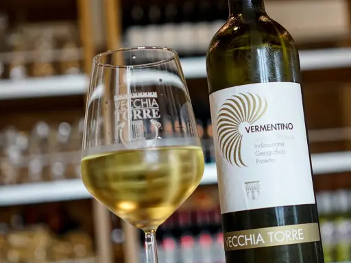 Un bicchiere di vino bianco Vermentino, frizzante e dorato, accanto alla sua bottiglia Vecchia Torre.