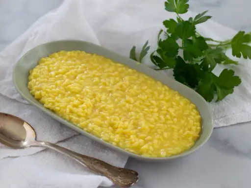 Un cremoso risotto al pistacchio, servito in un piatto ovale con un cucchiaio d'argento e un rametto di prezzemolo fresco.