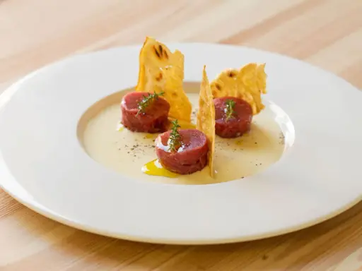 Tre cilindri di tartare di manzo, guarniti con timo, su una crema chiara e croccanti cialde. Un'idea su come condirla.