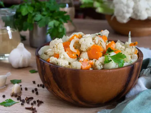 Un'appetitosa giardiniera in agrodolce, con cavolfiore, carote e cipolle, servita in una ciotola di legno.