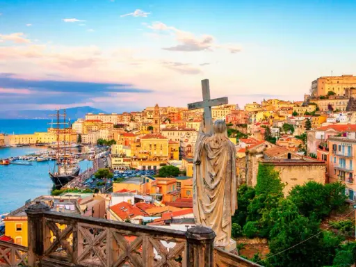 Statua con croce domina la vista di Gaeta, perfetta per una gita fuori porta da Roma. Porto, case colorate e castello sullo sfondo.