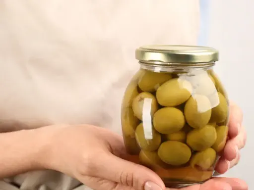 Mani che tengono un barattolo di olive verdi in salamoia per olive, pronte per essere gustate.