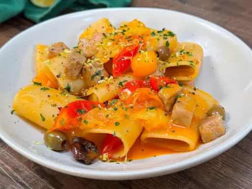 Paccheri con tonno fresco, pomodorini, olive e scorza di limone. Un piatto colorato e saporito, pronto per essere gustato.