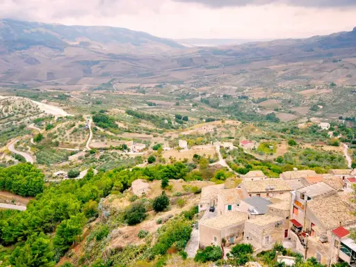 Panoramica di Contessa Entellina, un borgo siciliano tra colline verdi e campi coltivati, con case dai tetti in cotto e una strada tortuosa.