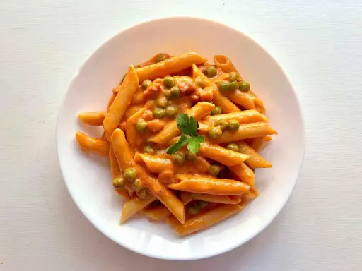 Penne ai 7 peccati: un piatto di pasta cremosa con piselli e un tocco di pomodoro, guarnito con prezzemolo fresco.