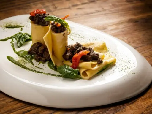 Pappardelle alla lepre, un piatto ricco e saporito, con pasta fresca, ragù scuro e guarnizioni verdi.