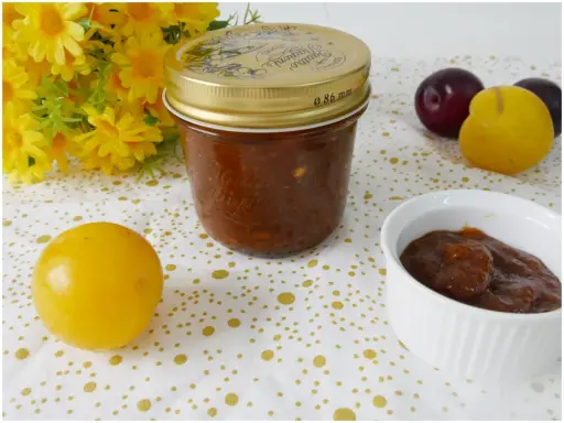 Vasetto di marmellata di susine fatto in casa, con prugne rosse e gialle e fiori gialli sullo sfondo.