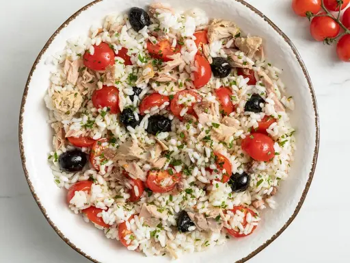Insalata di riso con tonno, pomodorini, olive nere e prezzemolo. Un'idea fresca e gustosa su come condire l'insalata di riso per un pranzo estivo.