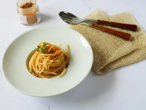 Spaghetti alla bottarga, un piatto semplice ma gustoso, pronto per essere assaporato. Un vasetto di bottarga in polvere e posate completano la scena.