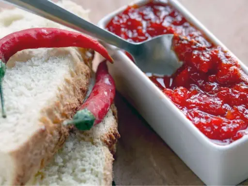 Fette di pane con peperoncini rossi e una ciotolina di marmellata di peperoncino, pronta per essere gustata.