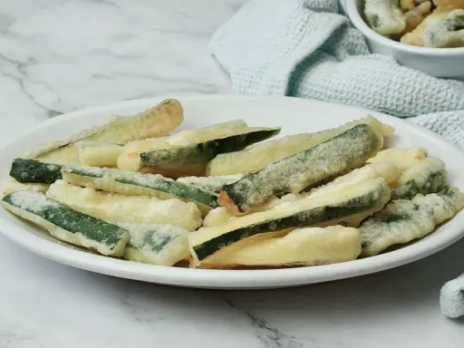 Zucchine fritte in pastella dorata, croccanti e invitanti, servite su un piatto bianco.