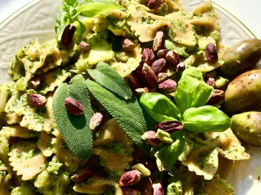 Farfalle condite con un saporito pesto di salvia, guarnite con pistacchi, basilico e olive verdi.
