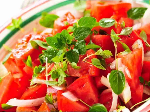 Un'insalata di pomodori freschi e succosi, condita con cipolla bianca e profumata erba aromatica.