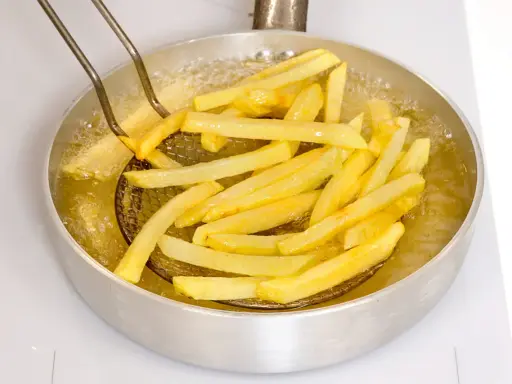 Patate fritte dorate che sfrigolano nell'olio bollente, pronte per essere gustate.