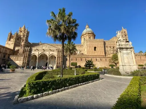 Il percorso per Palermo inizia con la maestosa Cattedrale, tra palme e giardini curati, sotto un cielo azzurro.