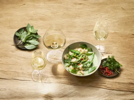 Un curry verde con gamberi e verdure, accompagnato da bicchieri di vino bianco, evoca le fresche **sauvignon blanc caratteristiche**.