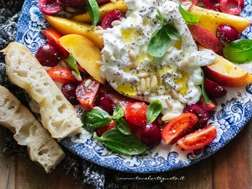 Insalata estiva con burrata, pesche, ciliegie, pomodorini e basilico, condita con olio e pinoli. Accompagnata da pane casereccio.