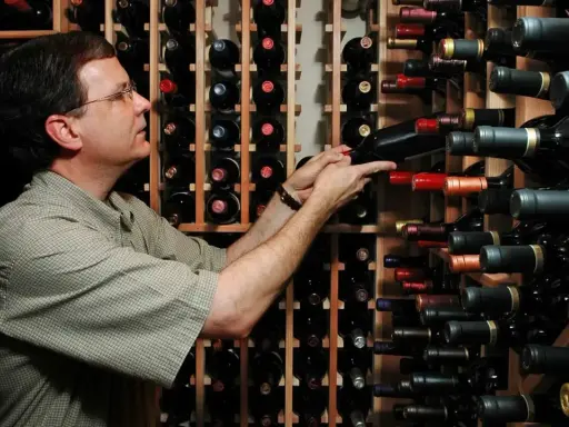 Uomo in cantina sceglie una bottiglia, pensando se il suo chardonnay è fermo o frizzante.