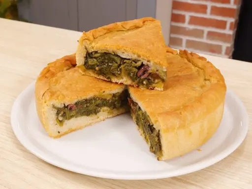 Una fetta di pizza di scarola, ricca di verdure e olive, su un piatto bianco.