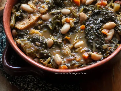 Un piatto fumante di ribollita toscana, con fagioli cannellini, cavolo nero e pane raffermo in un'autentica ciotola di terracotta.