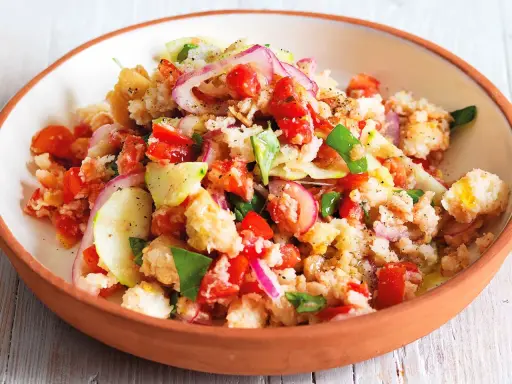 Panzanella ricetta: un'insalata estiva con pane raffermo, pomodori, cetrioli, cipolla rossa e basilico, condita con olio d'oliva.