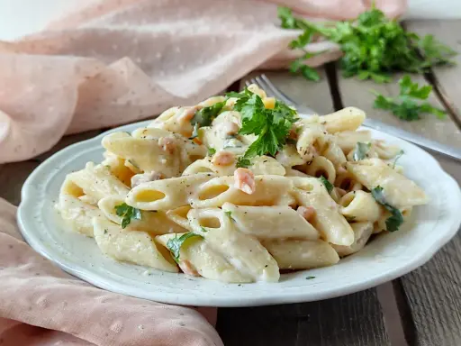 Piatto di pasta panna e salmone, guarnito con prezzemolo fresco, servito su un piatto bianco.