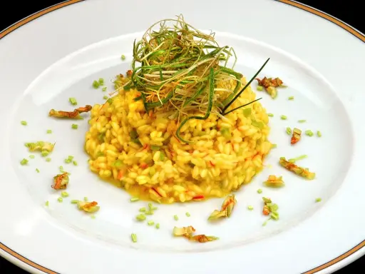 Risotto giallo intenso con fiori di zucca e zafferano, guarnito con erbe croccanti.