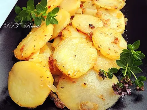 Patate e cipolle in padella, dorate e profumate, guarnite con rametti di origano fresco.