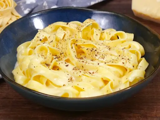 Un piatto di fettuccine alfredo fumanti, condite con una cremosa salsa al parmigiano e pepe nero.