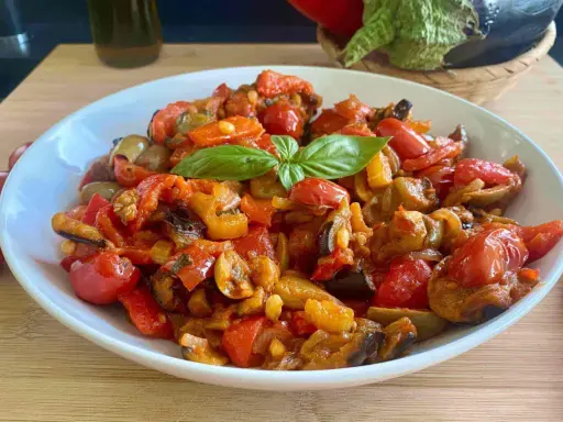Caponata siciliana ricetta della nonna: un piatto colorato con melanzane, peperoni, pomodorini e basilico, pronto per essere gustato.