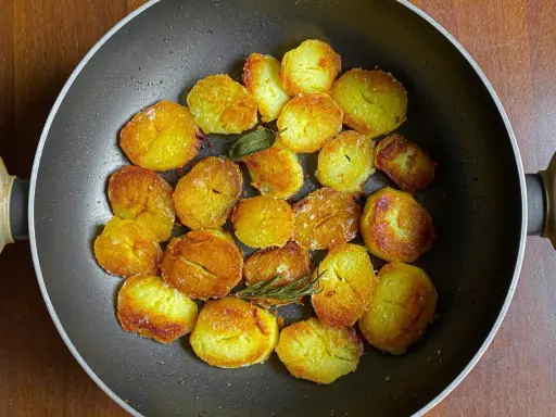 Patate dorate e croccanti in padella, pronte per deliziose ricette con patate. Un rametto di rosmarino aggiunge profumo.