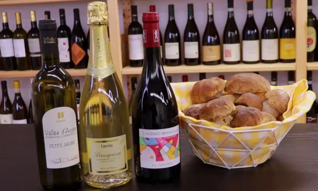 Vino da abbinare ai funghi: una bottiglia di rosso e due spumanti con un cesto di funghi porcini freschi.