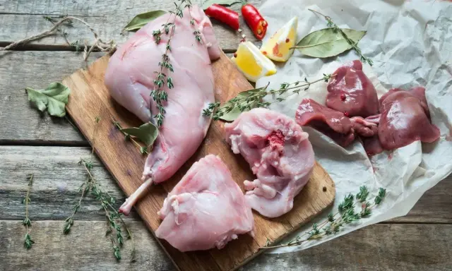 Coniglio crudo a pezzi su tagliere di legno, con erbe aromatiche, limone e peperoncino. Perfetto per un vino da abbinare al coniglio.