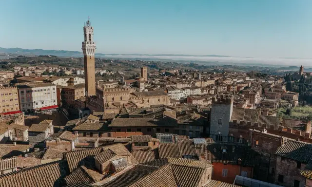 Vista aerea di Siena, con la Torre del Mangia in primo piano. Un'idea per cosa vedere in Toscana in 2 giorni, tra tetti in cotto e colline nebbiose.
