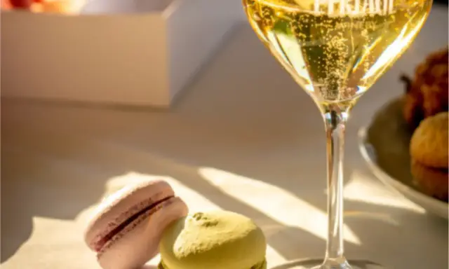 Un bicchiere di spumante frizzante, due macarons colorati e una scatola bianca. Un perfetto abbinamento cibo vino per un momento di dolcezza.