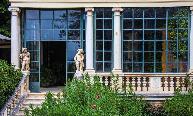 Statue di nani custodi di un giardino lussureggiante sui Colli Berici, con un'elegante serra sullo sfondo.