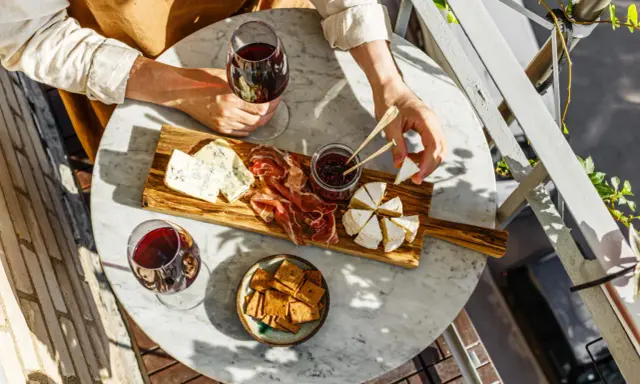 Un tagliere con formaggi, salumi e marmellata, accompagnato da un bicchiere di vino rosso. Le caratteristiche del nebbiolo vino si esaltano con questi sapori.