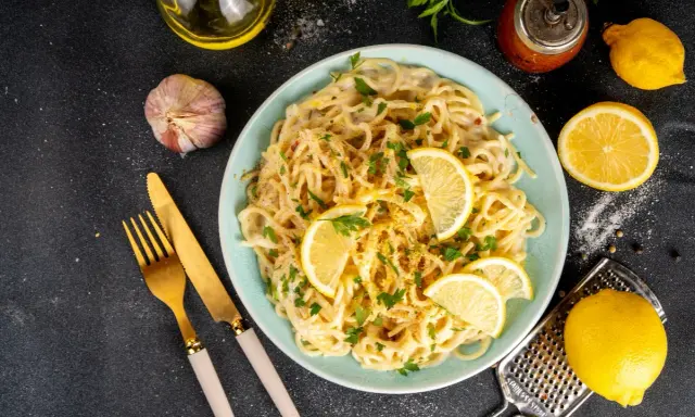 Spaghetti cremosi con un profumo agrumato, guarniti con fette di limone fresco e prezzemolo. Un piatto di pesto al limone che invita a gustare la freschezza.