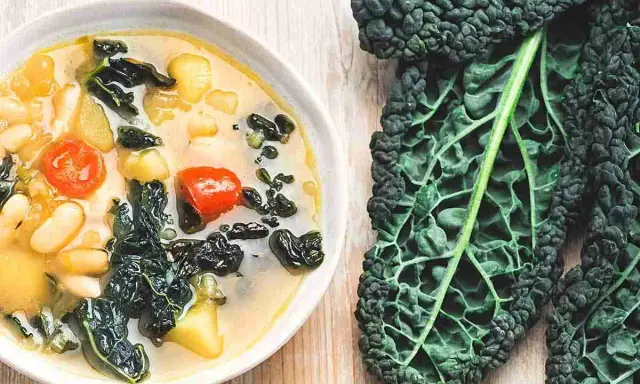 Zuppa ricca con fagioli, pomodoro e il sapore intenso del cavolo nero. Accanto, una foglia di cavolo nero fresca.