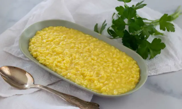 Un cremoso risotto al pistacchio, servito in un piatto ovale con un cucchiaio d'argento e un rametto di prezzemolo fresco.